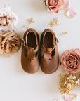 Medium brown leather Mary Janes for girls with floral detail.