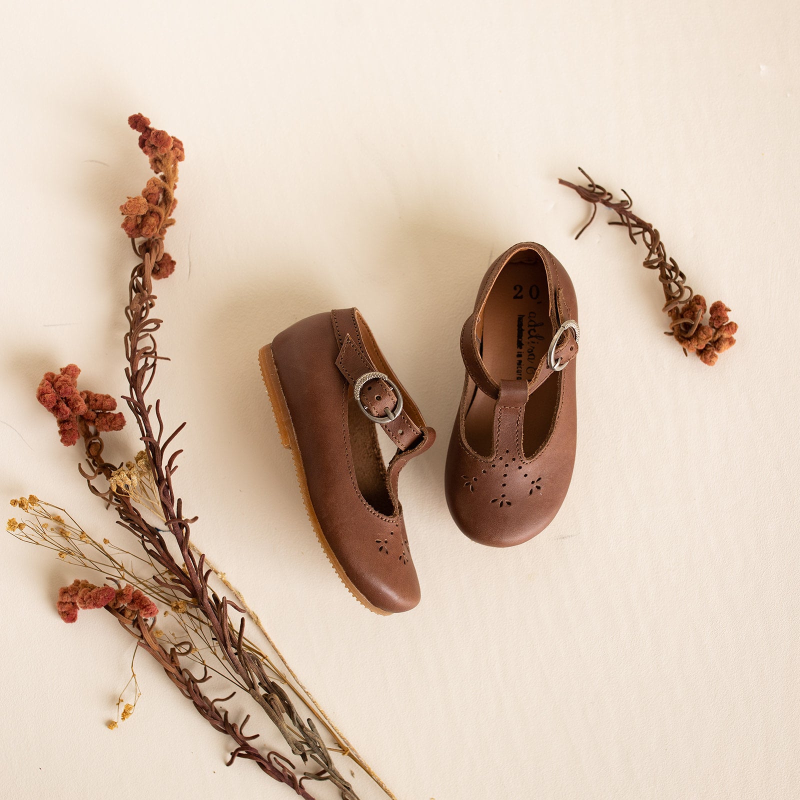 Adelisa &amp; Co t-bar Mary Janes with delicate floral detailing in dark brown leather. These leather Mary Jane shoes for girls are handmade and feature a buckle closure.