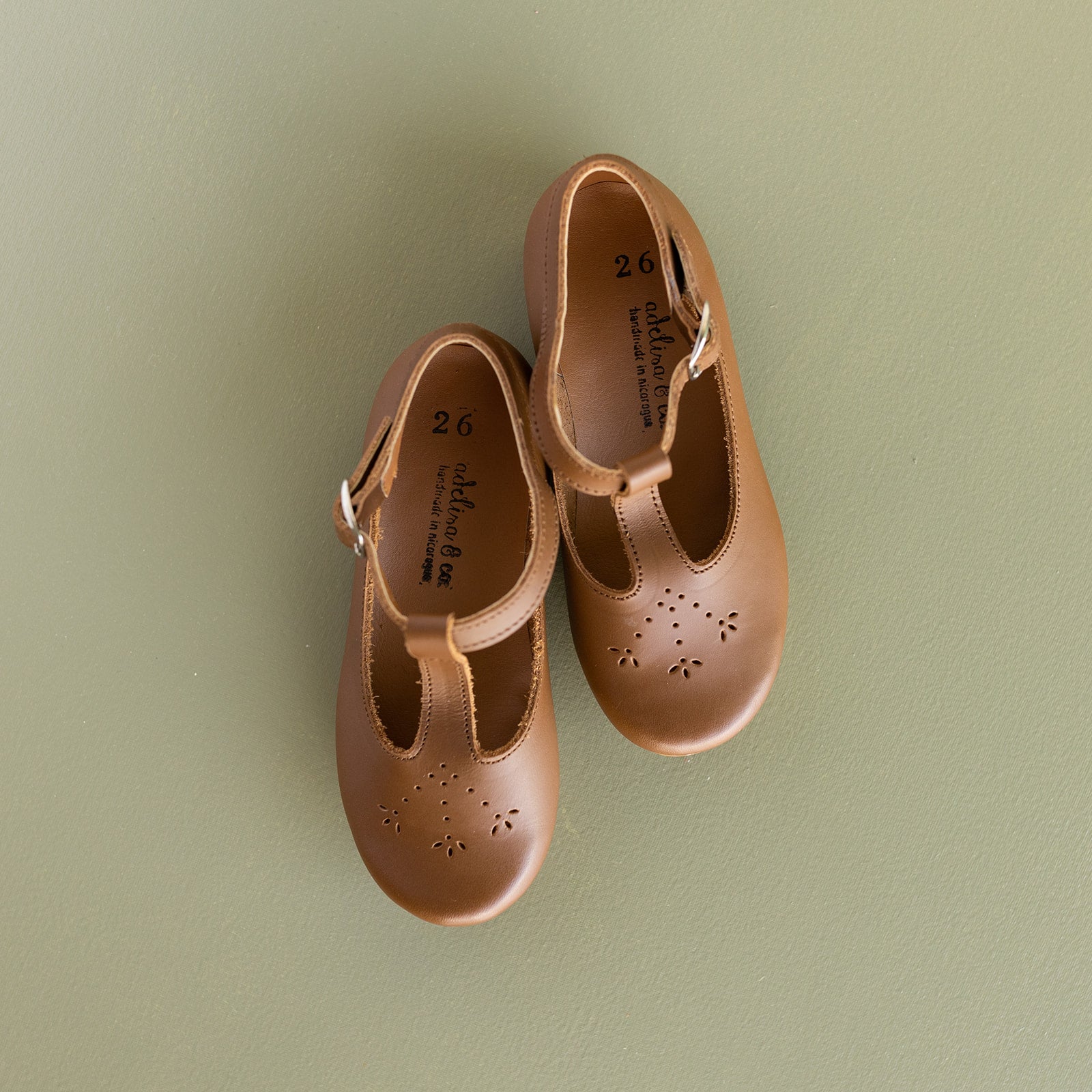 Adelisa &amp; Co t-bar Mary Janes with delicate floral detailing in medium brown leather. These leather Mary Jane shoes for girls are handmade and feature a buckle closure.
