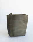 Small sized leather tote for children with a front pocket in an earthy, dark green leather.