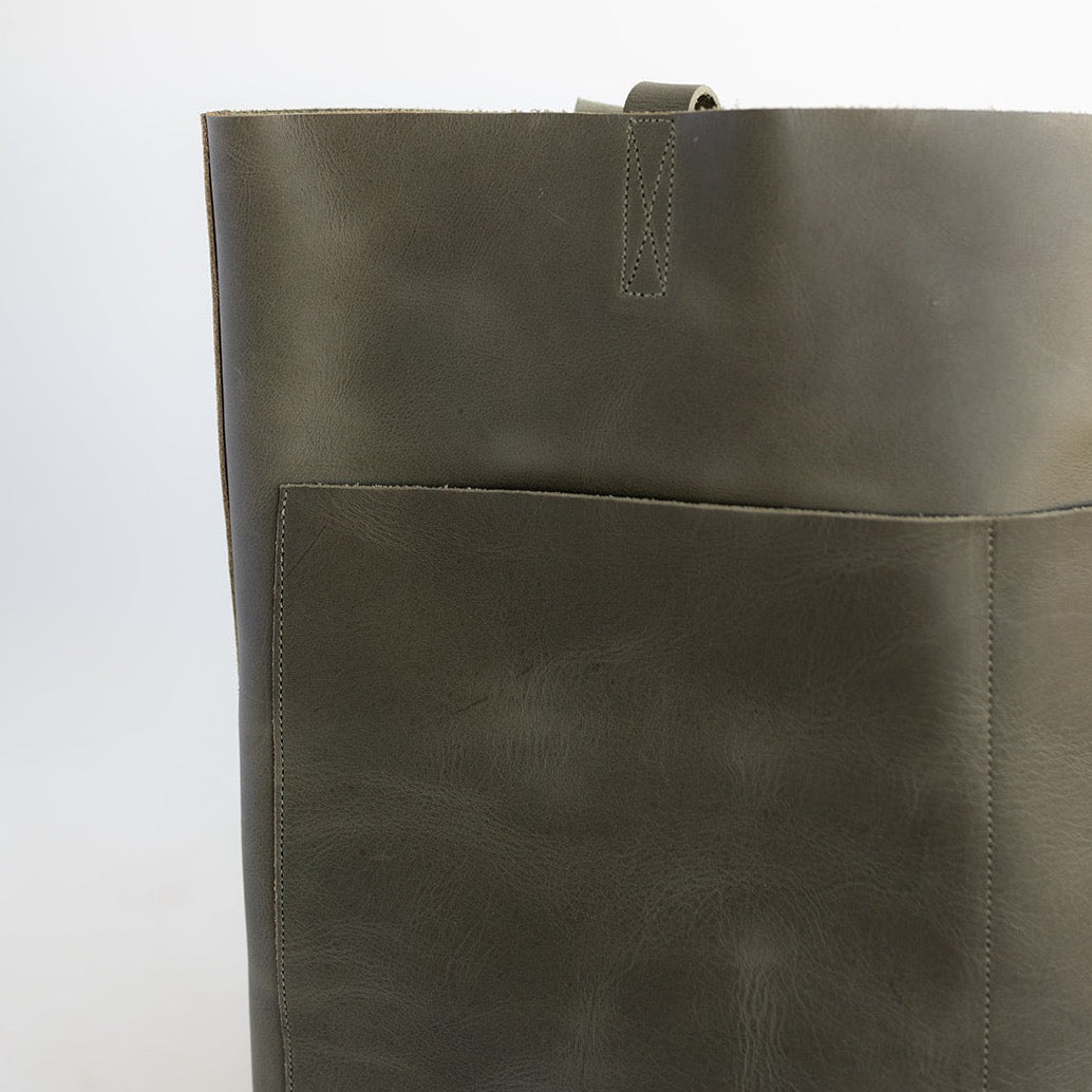 Large Women&#39;s leather tote with two front pockets and no hardware in an earthy, dark green leather.