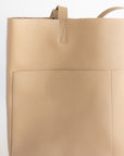 Large women's handmade leather tote in beige with two front pockets.