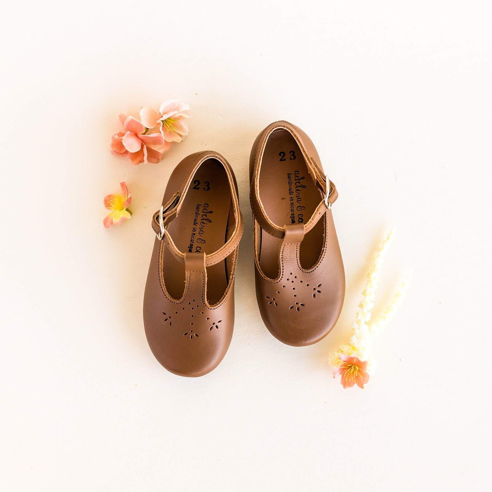 Adelisa & Co t-bar Mary Janes with delicate floral detailing in medium brown leather. These leather Mary Jane shoes for girls are handmade and feature a buckle closure. 